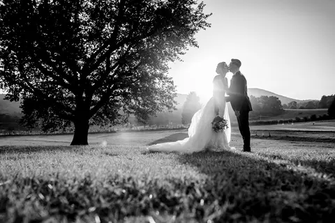 La sposa Erika e lo sposo Luca si baciano sotto un albero in un campo aperto.
