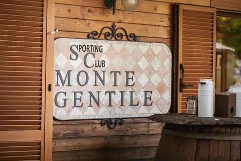 Segno del Sporting Club Monte Gentile con parete in legno e shutters aperti.