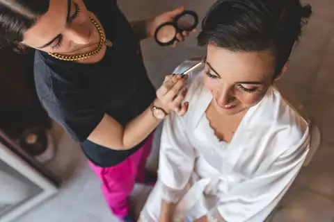 La truccatrice sistema il make-up della sposa in accappatoio bianco