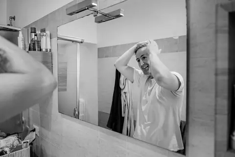 Lo sposo si sistema i capelli davanti allo specchio del bagno, in bianco e nero