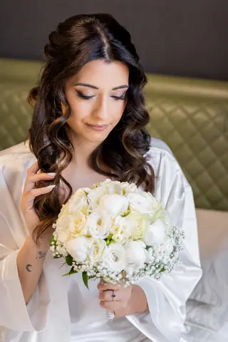 La sposa in vestaglia tiene il bouquet di rose bianche a occhi bassi