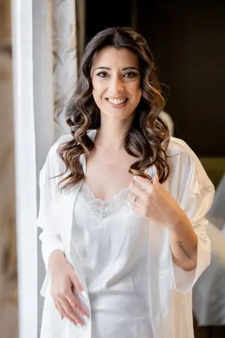 Ritratto sorridente della sposa in vestaglia di raso davanti alla finestra