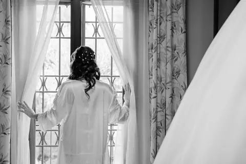 La sposa di spalle alla finestra, tra le tende della camera