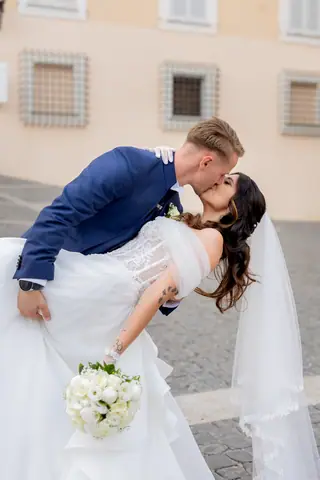 Gli sposi si baciano davanti al palazzo storico, con il bouquet in primo piano