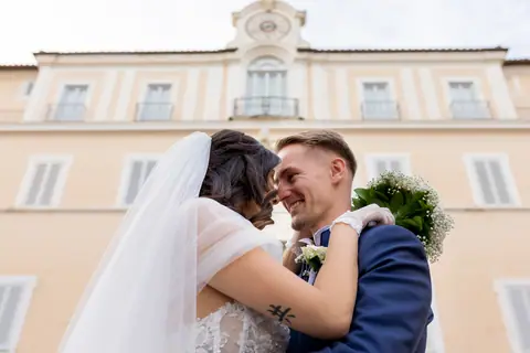Gli sposi abbracciati sotto il velo davanti alla facciata del palazzo