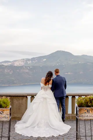 Gli sposi di spalle sulla balconata guardano il lago e le montagne