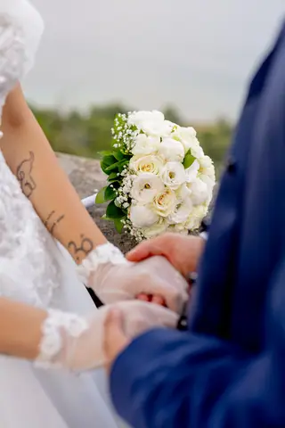 Dettaglio delle mani unite e del bouquet di rose bianche
