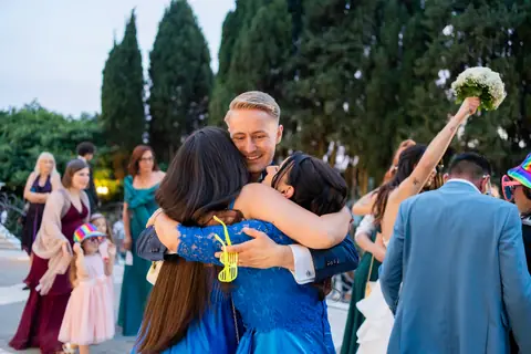 Gli invitati abbracciano gli sposi con il bouquet alzato in giardino