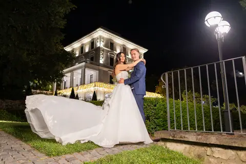 Gli sposi abbracciati in giardino davanti alla villa illuminata di notte