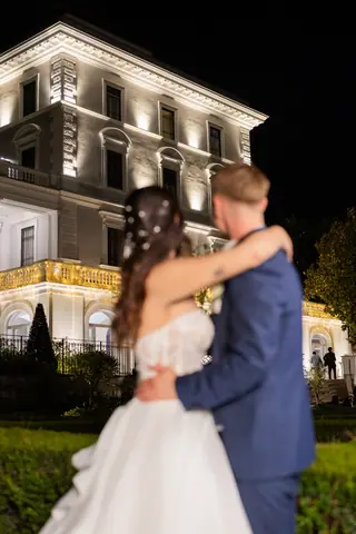 Gli sposi si abbracciano di notte con la facciata della villa alle spalle