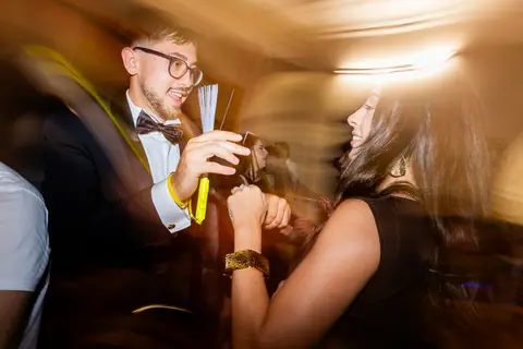 Due invitati ballano con i bicchieri in mano tra le luci della festa