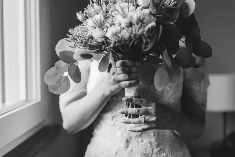 Le mani della sposa tengono il bouquet controluce, in bianco e nero