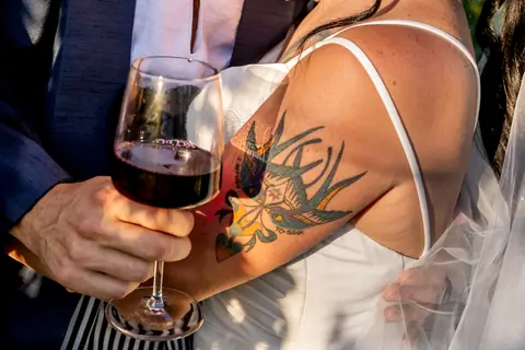 Dettaglio del calice di vino rosso e del tatuaggio della sposa