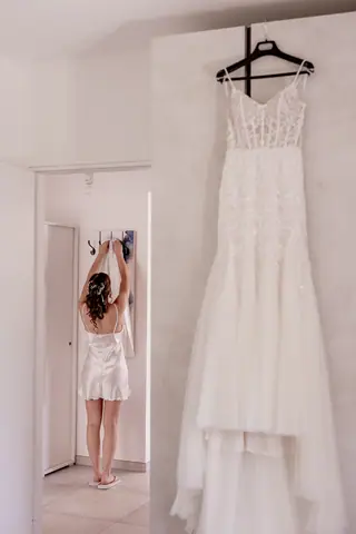 L'abito appeso e la sposa riflessa nello specchio in fondo alla stanza
