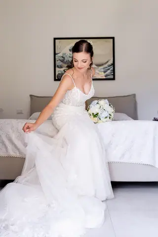 La sposa siede sul letto con l'abito e il bouquet