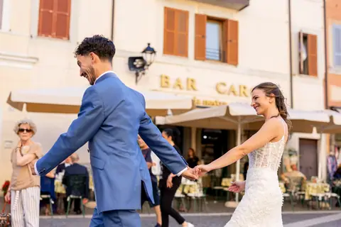 Gli sposi si tengono per mano tra i tavolini della piazza