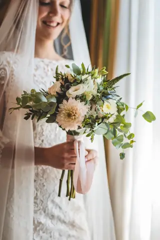 La sposa sorride con il bouquet in mano davanti alla tenda chiara