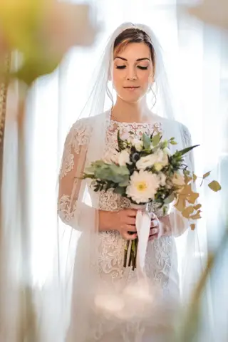 Ritratto della sposa con il bouquet in controluce davanti alla finestra