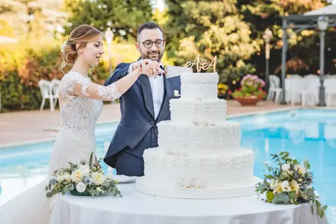 Gli sposi tagliano la torta a più piani accanto alla piscina